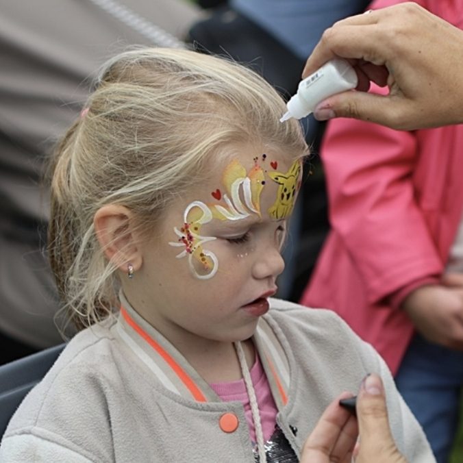 Een meisje krijgt een tatoeage met kleurstoffen op haar arm terwijl een volwassene helpt.