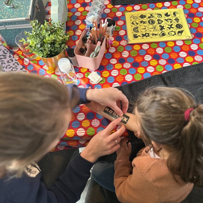 Een volwassene helpt een kind met het aanbrengen van een tattoo op de arm.