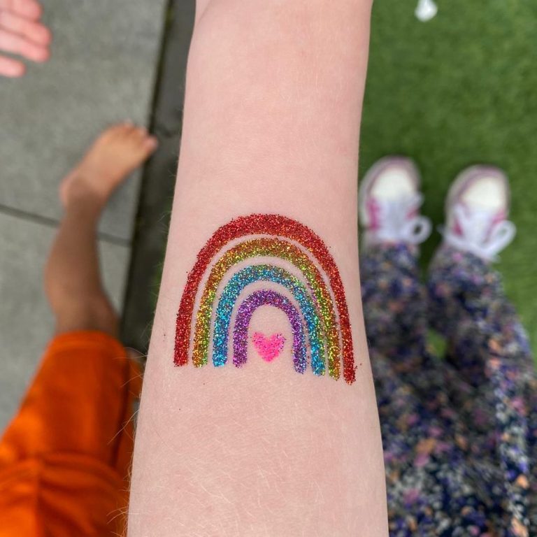 Kleurrijke glittertattoo van een regenboog met een hartje aan de onderkant.