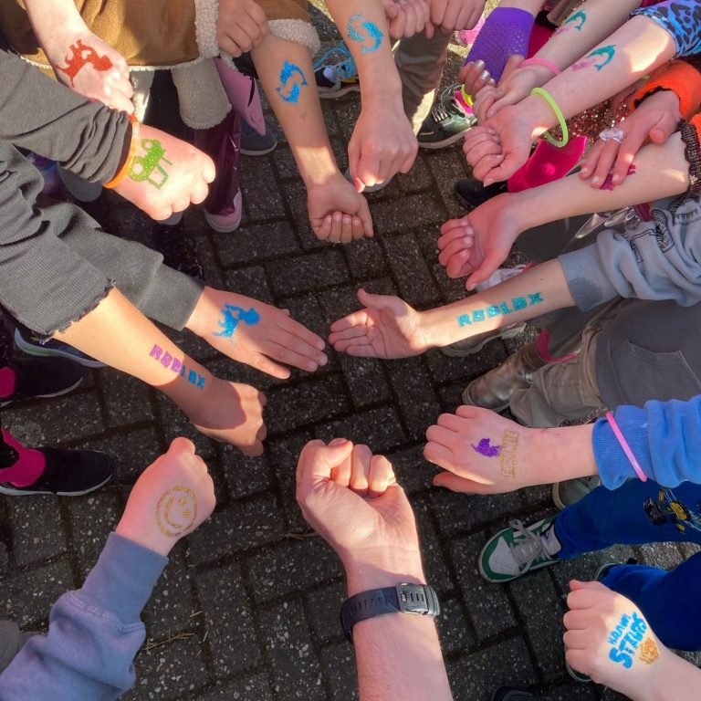 Een cirkel van handen met kleurrijke tekeningen op de onderarmen, in een speelse sfeer.