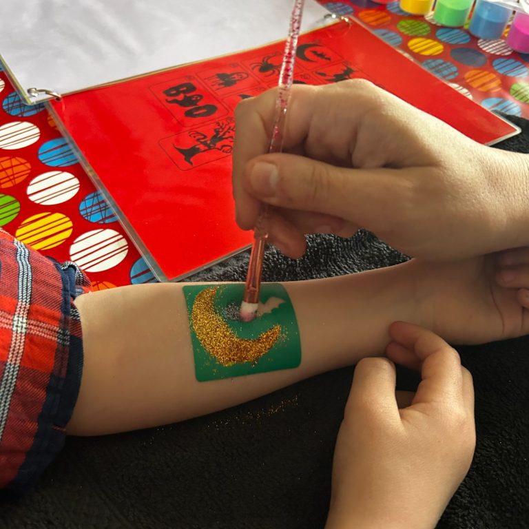 Een hand maakt een tijdelijke tattoo van een maansikkel op een arm.