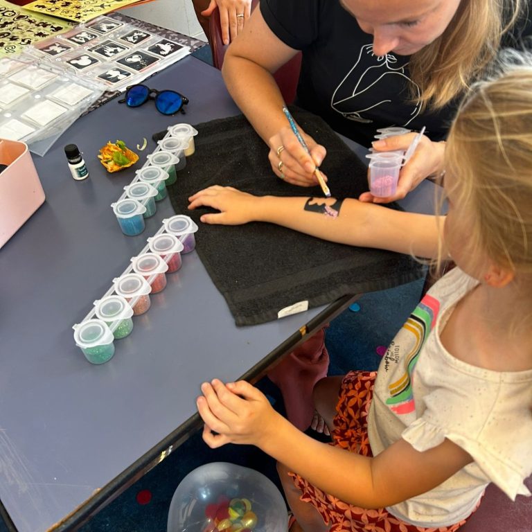 Een meisje krijgt een tatoeage met kleurstoffen op haar arm terwijl een volwassene helpt.